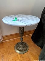 Full view of the round side table showing white marble top and brass base with openwork design.