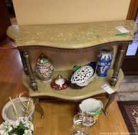Console table with two beige stone tiers, metal braces, and ornate metal legs, displayed from a front angle. Various decorative items on and around the table are excluded from sale.