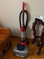 Photo of red Dirt Devil Quick-Lite vacuum cleaner standing vertically near wall and furniture