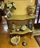 View of ceramic and glass vases arranged on a decorative two-shelf wooden table, including ceramic flower frog bowl and plant pot.