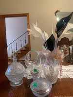 Overview of all glass items on table including two glass vases with glass flowers, a glass basket with handle, and two lidded glass bowls