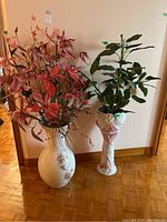 Two large floor vases placed side by side against wall, each holding faux flower arrangements with differing colors and styles.