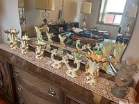 Four cream and gold pottery vases and two double candleholders on a wooden surface with a crocheted dresser scarf, mirror reflection showing part of the room
