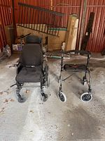 Photo shows black HME wheelchair with padded seat and armrests next to a black foldable walker with seat and front wheels, inside a garage with various items in background.