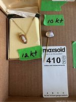 Photo showing the 12kt gold cameo pendant on chain in its display box and the 10kt gold stick pin next to it with a green tape label indicating metal karat.