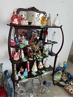 Front angle view of carved oak display cabinet with five wooden shelves supporting various ceramic figurines, top decorative carved crest, and mirrored back panel.