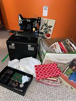 Portable Singer sewing machine in open black case, bin of patterns, fabric scraps and accessories visible