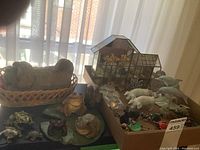 Overview of the collection on a table showing many animal figurines including frogs, turtles, squirrel, dog in basket, and glass greenhouse.