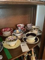 Six vintage porcelain cups and saucers displayed on wooden shelf showing variety of floral designs and gold trims