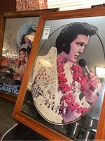 Photo of two wood framed mirrors, one with Elvis Presley image in white costume and red lei, the other with Battlestar Galactica characters.