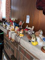 Multiple bird figurines, some with dangling legs, displayed on a fireplace mantle against wood paneling, showing a variety of ceramic and wood styles.