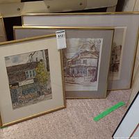 Three framed Gerard Paraghamian artworks leaning against wall showing varied Toronto urban scenes.