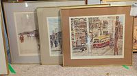 Three framed prints by Gerard Paraghamian leaning against a wall, depicting Toronto scenes and Peggy's Cove.