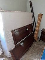 Photos showing the disassembled solid wood double bed components including headboard, footboard, rails, slats, mattress, and box spring. Also visible are some wooden planks and a nightstand.