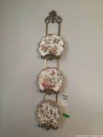 Full view of ornate wall-mounted metal plate rack displaying three scalloped-edge floral plates.