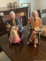 Photo of two Royal Doulton figurines side by side on a dark wooden table.