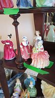 Four Royal Doulton porcelain figurines displayed on a wooden shelf. Each figure shows detailed painting and glossy finish.