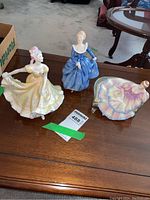 Three Royal Doulton figurines displayed on table including Ninette, Fragrance, and Pauline