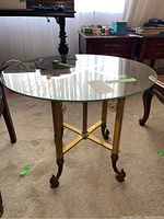 Full view of side table showing round glass top and brass base with ornate legs and claw feet.