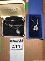 Both pendants displayed in their respective boxes with chains, showing detailed design and brand markings.