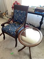 Photo showing the oval side table with wooden Duncan Phyfe style frame and removable glass top beside the vintage armchair with floral upholstery.