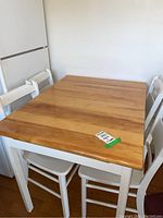 Dining table with natural wood top and white painted base, surrounded by four matching white painted ladder back chairs placed around the table.