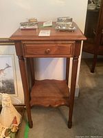 Solid wood telephone table with drawer shown from front with decorative silver metal boxes on top.