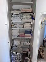 Tall shelf filled with multiple stacks of folded linens, towels and sheets in various colors and patterns, with a zebra print hamper at the bottom