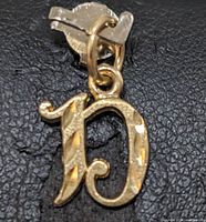 Close-up image showing the front of the 10K yellow gold initial 'D' pendant, highlighting its polished and textured surface.