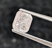 Diamond held in tweezers showing cushion shape and internal inclusions