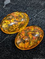 Close-up of two oval amber gemstones showing natural internal organic inclusions and polished surfaces on a dark fabric background.