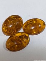 Three polished oval amber cabochons with natural inclusions visible on white background