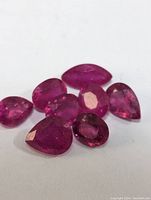 Seven loose, faceted ruby gemstones of varying cuts and sizes shown on white background.