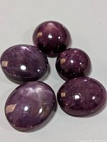 Five polished genuine star ruby cabochon gemstones showing star effect and varied purplish-red coloration.