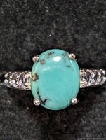 Front view of the ring showing large oval turquoise stone with brown matrix and tanzanite accented band on black background.