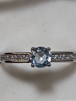 Close-up top view of the sterling silver ring showing the blue topaz center stone and clear accent stones on the band.