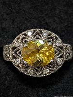 Close-up image of the top view of a sterling silver ring with a faceted oval yellow citrine center stone and filigree surrounding design with small accent stones.