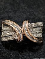 Close-up photo showing sterling silver ring with multi-row round CZ and baguette CZ swirl design on black background.