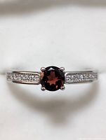 Front view of sterling silver ring with round garnet center stone and accent stones on band.