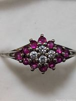 Close-up front view of the ring showing the cluster of red and clear round gemstones set in sterling silver.