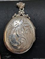 Front view of sterling silver oval locket pendant showing detailed engraved floral and scroll design.