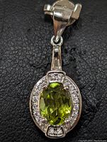 Front view of the sterling silver pendant featuring an oval green peridot gemstone surrounded by small clear stones.