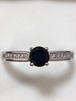 Close-up front view of the sterling silver ring showing the round dark blue sapphire center stone with small clear stones along the band.