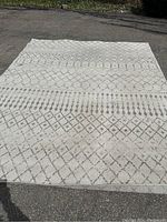 Full view of cream and grey area rug with geometric pattern laid flat on pavement.