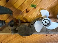 Three boat propellers displayed on a wooden surface against a wood wall. Includes two vintage brass props and one white aluminum prop.