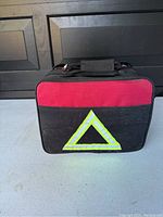 Photo showing the front of the red and black fabric soft carrying case with reflective triangle symbol.
