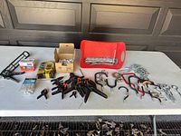 Wide shot of entire lot showing clamps, hooks, screws, chain, measuring tape, and a small hand tool on gray surface.