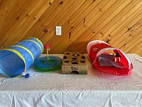Photo showing full set of cat entertainment items including two cat tunnels (blue and red), a round ball chase toy, and a square puzzle box.