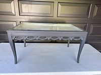 Front view of coffee table showing rectangular glass top, carved apron detail, and curved legs.