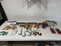 Photo showing assortment of crafts supplies and carpentry accessories arranged on white table including sea glass pieces, wood stumps, rope, hooks, drawer pulls, screwdrivers, caulking guns, glue, nails, and level.
